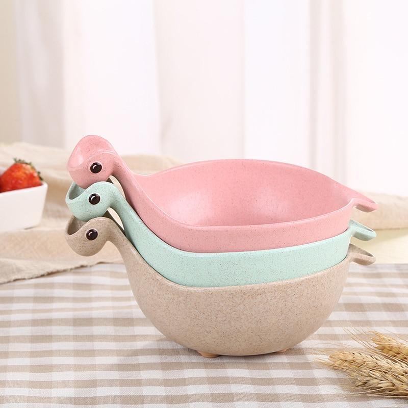 Stackable dinosaur-shaped bowls in pink, green, and beige on a striped surface.
