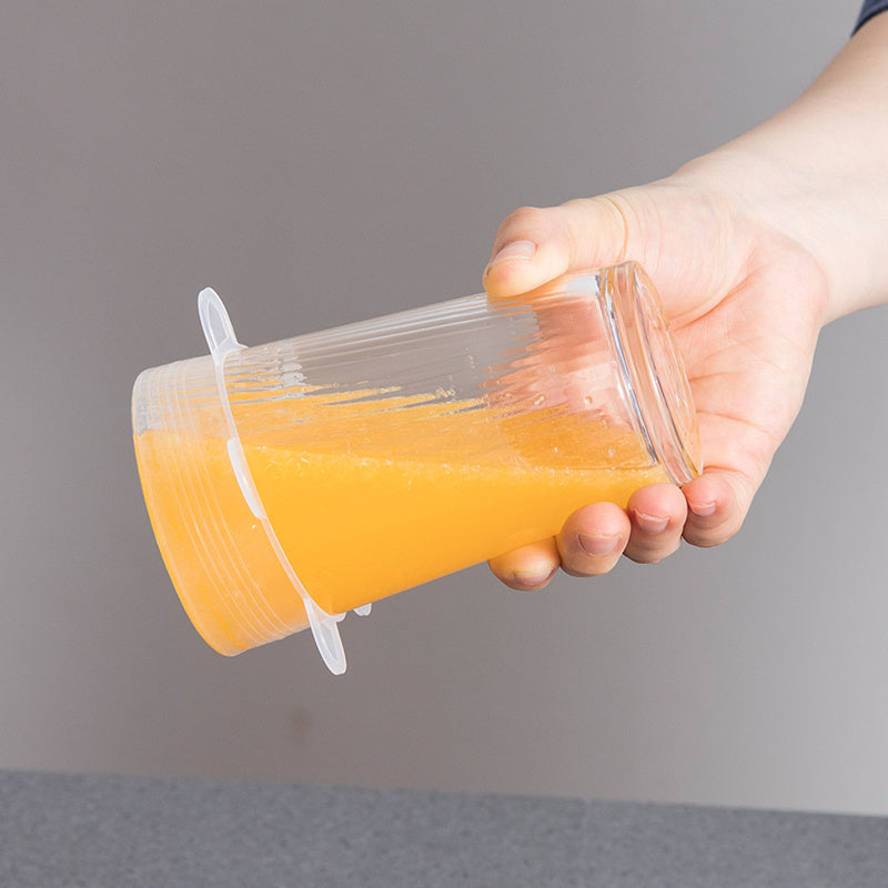 Hand holding a clear plastic cup with orange juice against a gray background